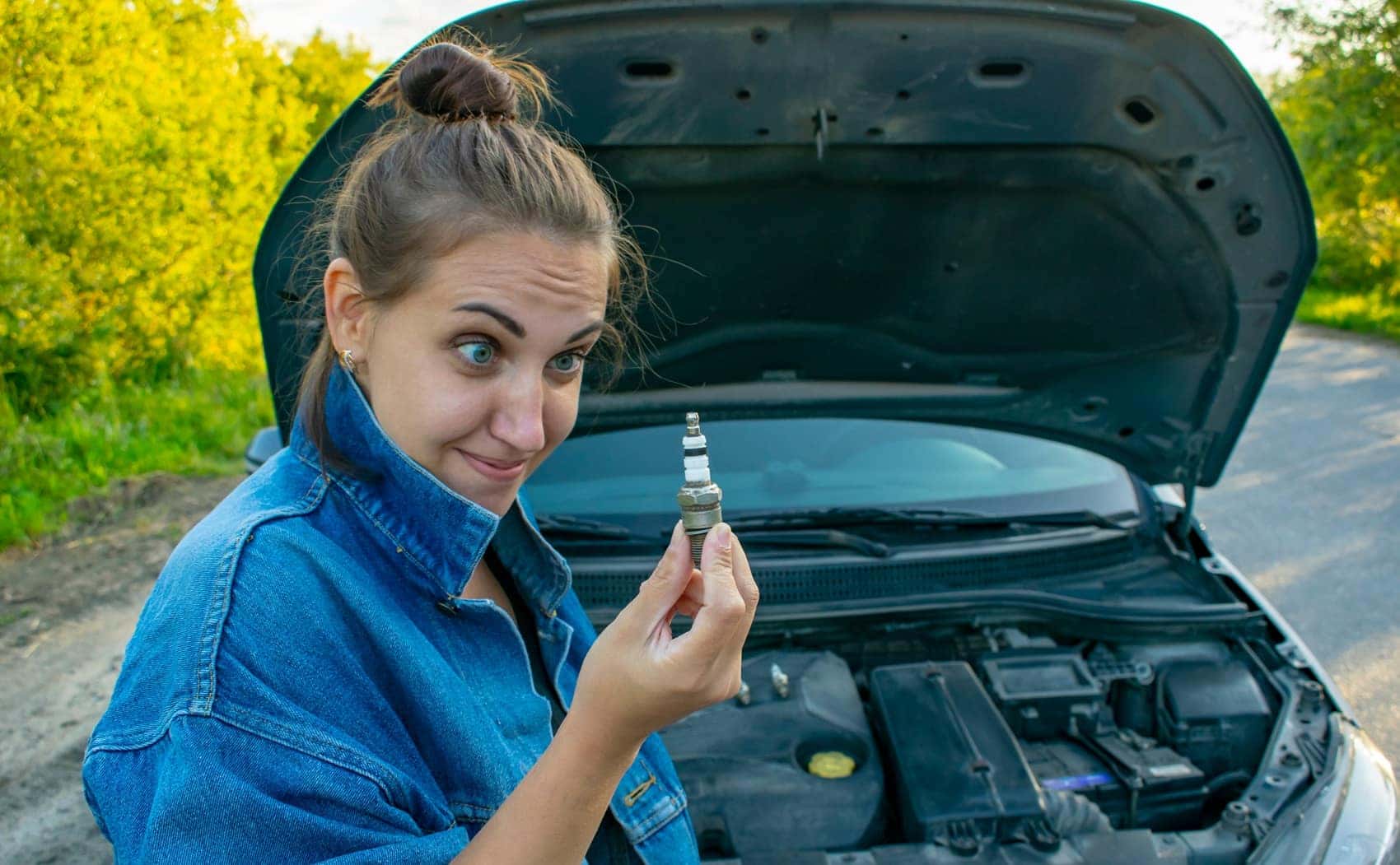 Woman looking at spark plug while car hood is up