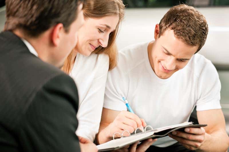 Couple signing paperwork as dealer holds car keys
