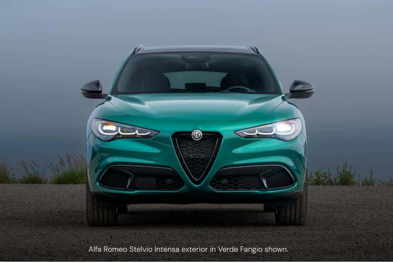 Front view of an Alfa Romeo Stelvio in Verde Fangio highlighting its signature V-shaped grille on a coastal road.