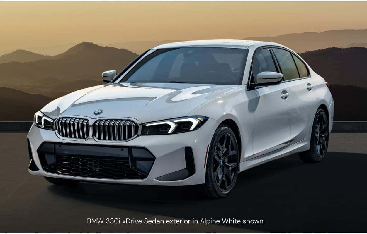 Three-quarter front view of a BMW 330i xDrive Sedan in Alpine White showcasing its black alloy wheels.