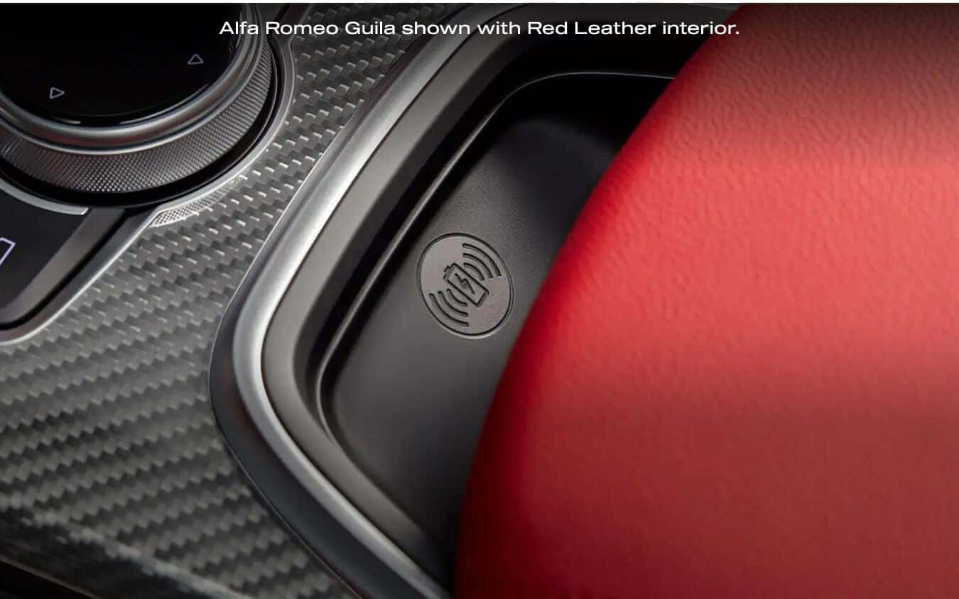Close-up view of the wireless charging pad and carbon fiber trim in a 2026 Alfa Romeo Giulia with Red Leather interior.