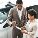 Dealer and customer completing paperwork next to a white car