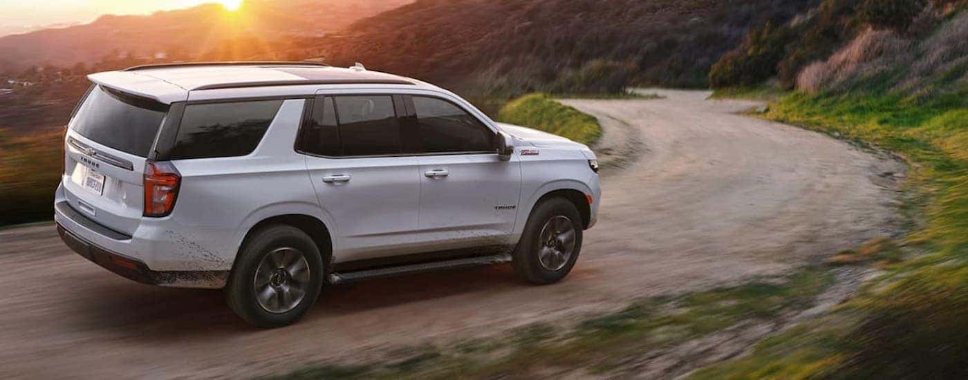 A white 2021 Chevy Tahoe is shown from the side driving on a dirt road after leaving a used Chevrolet dealer.