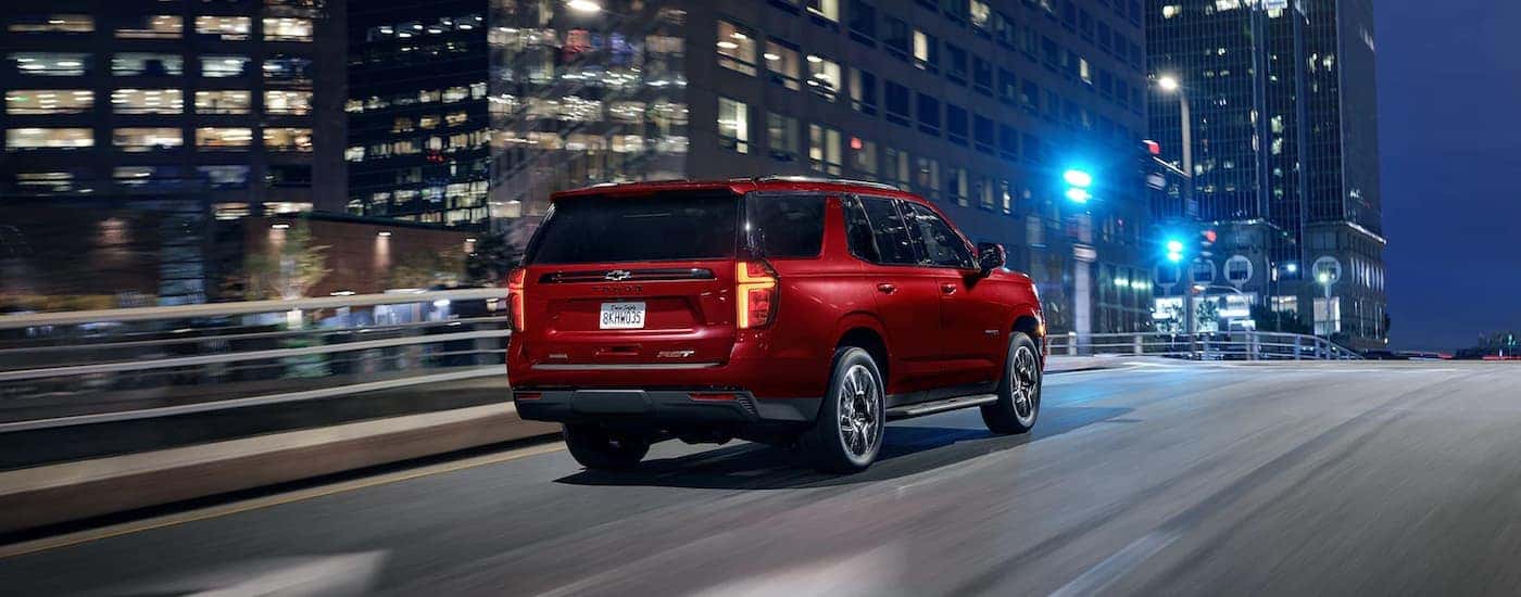 A red 2023 Chevy Tahoe RST driving on a city highway at night.