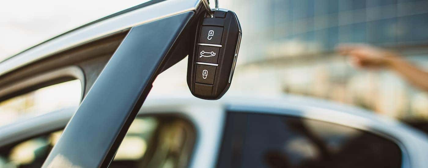 A car key is hanging off of an open car door.