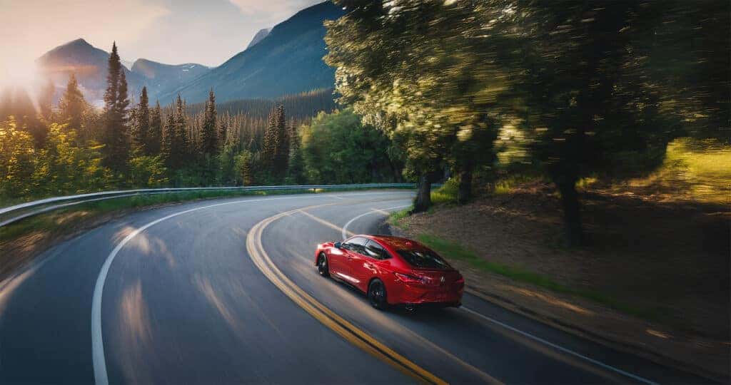 A Performance Red Pearl 2026 Acura Integra A-Spec driving through the Rocky Mountains at sunset