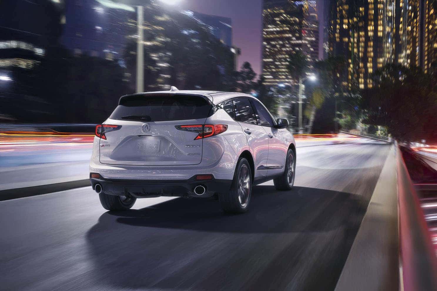 2026 Acura RDX in white driving through a downtown city at night
