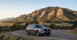 2026 Acura RDX driving on a scenic road with the Flatirons near Boulder, Colorado in the background, highlighting luxury SUV styling in a mountain setting