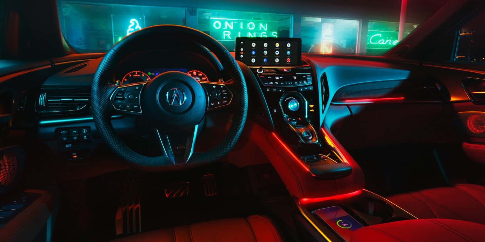 2026 Acura RDX interior view showing the driver-focused cockpit, Acura steering wheel, digital display screen, center console controls, and red ambient lighting.
