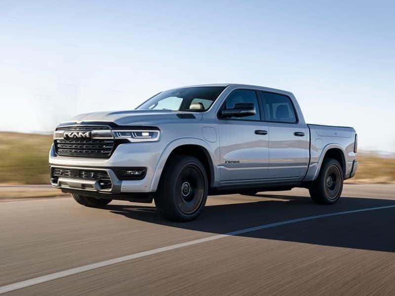 A gray Ram 1500 drives along a road during a sunny day.
