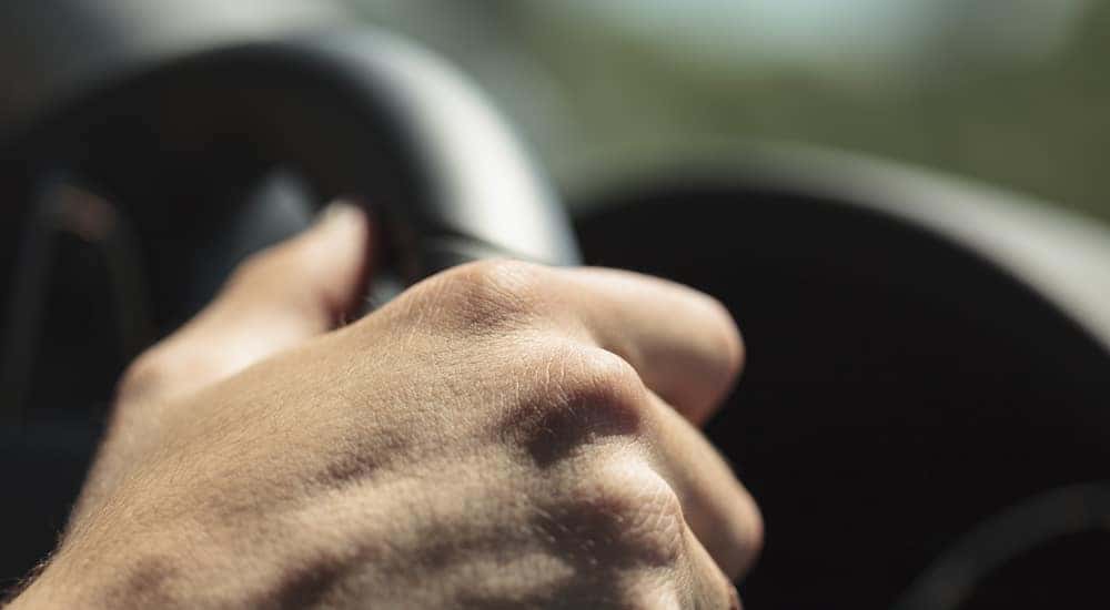 Close-up of a hand wrapped around a black steering wheel