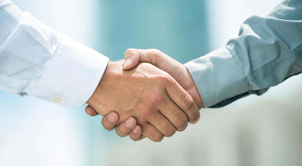 Close-up of man in a white shirt shaking hands with a man in a blue shirt