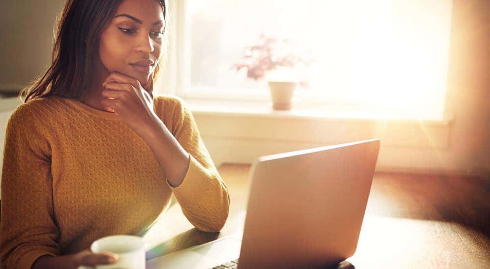 Woman in a yellow sweater sitting at her desk using a laptop with her hand on her chin