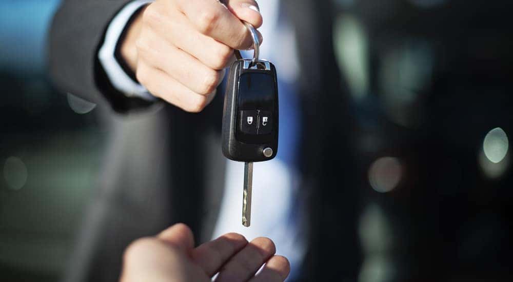 Man in a black suit and white button-up placing a black car key in an open hand