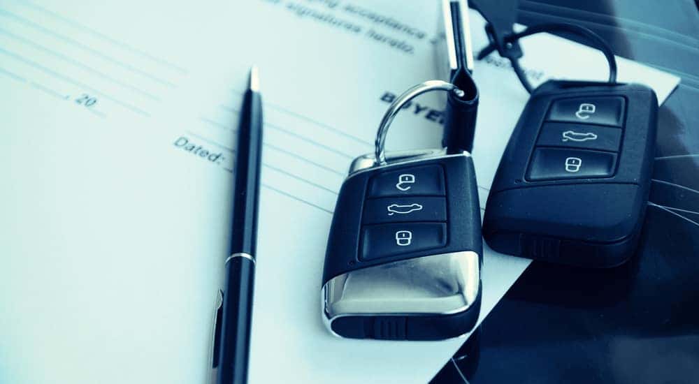 Two black car keys next to a black pen on top of a contract