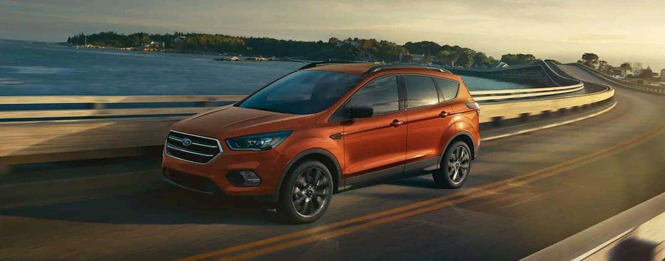 An orange 2019 Ford Escape driving over a bridge at sunset