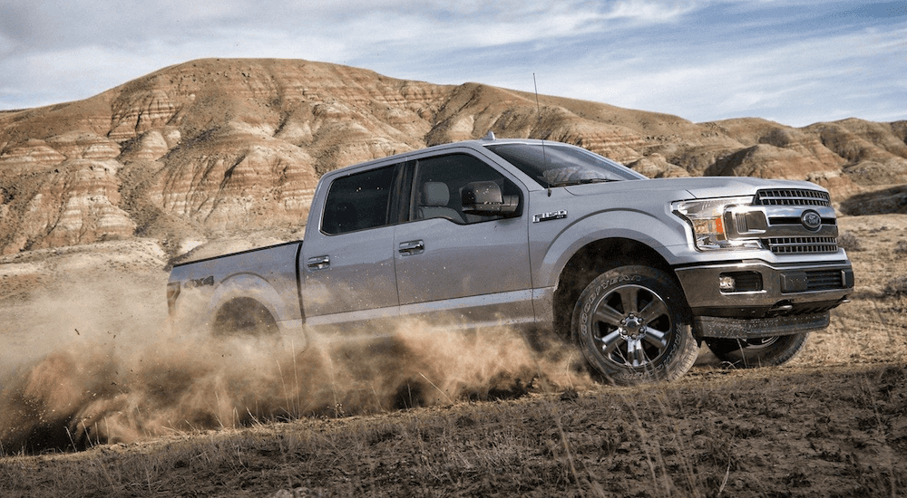 Silver 2019 Ford F150 driving on dirt road with mountain in back