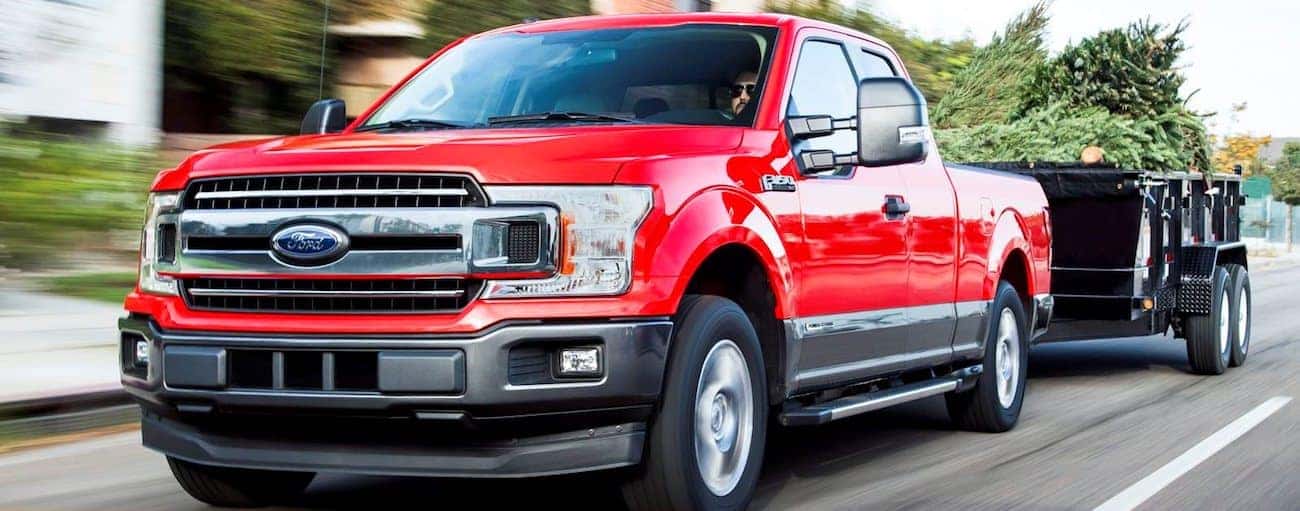 A red 2019 Ford F-150 tows a black metal trailer down a suburban street