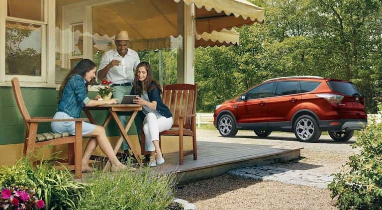 A man and two women sitting in front of a cafe with red/orange 2019 Ford Escape in back