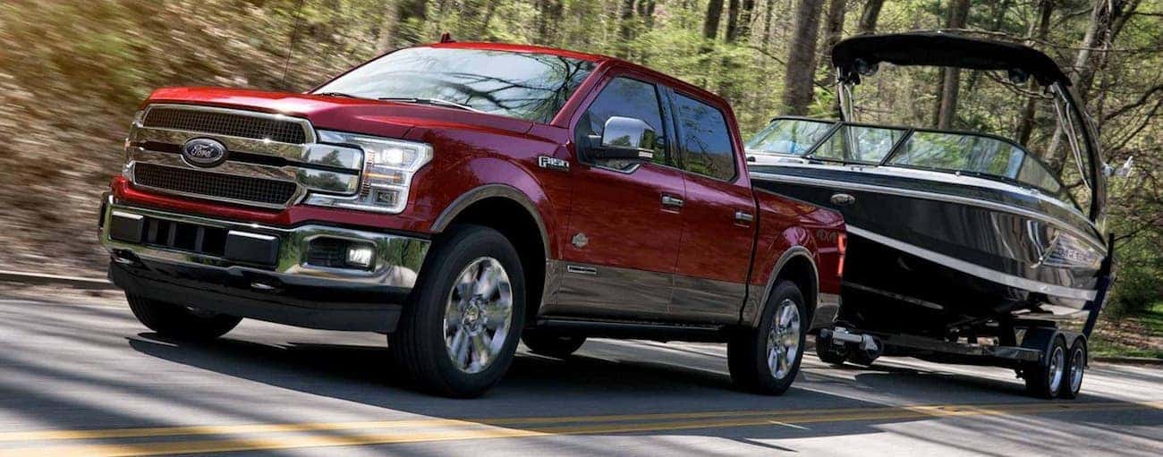 Dark red 2019 Ford F150 towing boat on wooded road