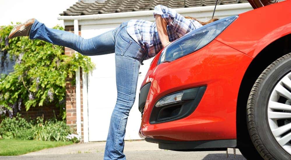 Red car with hood open, woman leaning in to inspect engine
