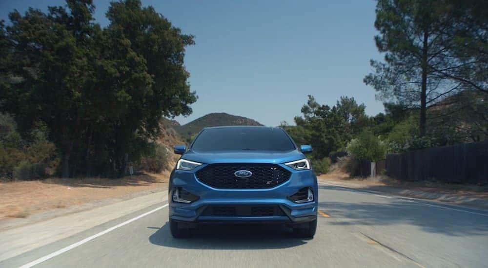 A blue 2019 Ford Edge from the front races down an empty road against a clear blue sky