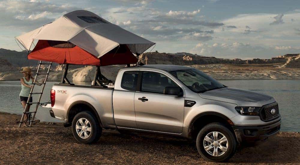 A woman climbs into a truckbed tent on a silver 2019 Ford Ranger at a lake