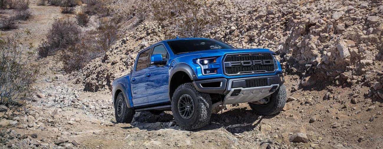 A blue Ford F150 Raptor climbing over rocks