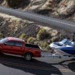 A red 2019 Ford Ranger tows a boat up a mountain road