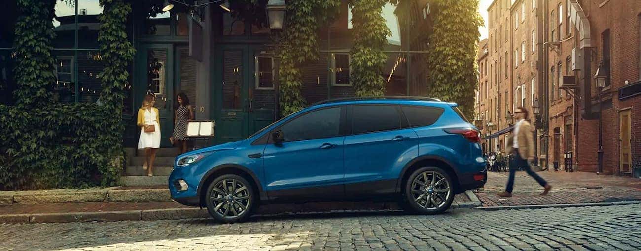A blue 2019 Ford Escape is parked on a cobblestone street in front of shops.