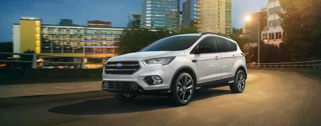 A white 2019 Ford Escape is driving away from a city at a darker hour. Compare the 2019 Ford Escape vs 2019 Chevy Equinox for performance.
