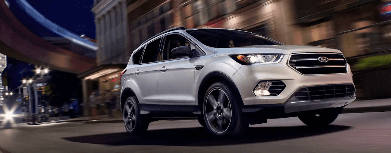 A white 2019 Ford Escape is taking a corner at night in the city.