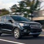 A black 2019 Escape, one of the Ford SUVs available in Cincinnati, OH, is driving in front of a shop.