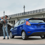 A young coupe is taking a selfie in front of their blue 2019 Ford Fiesta that they got with Ford lease deals in Cincinnati, OH.