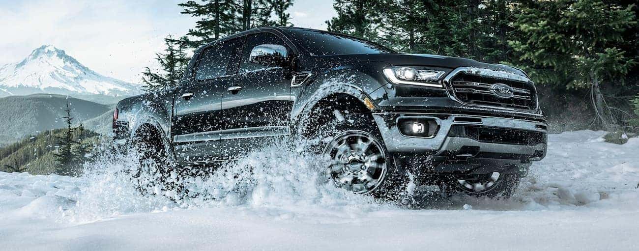 A black 2019 Ford Ranger is driving in the snow in front of mountains.