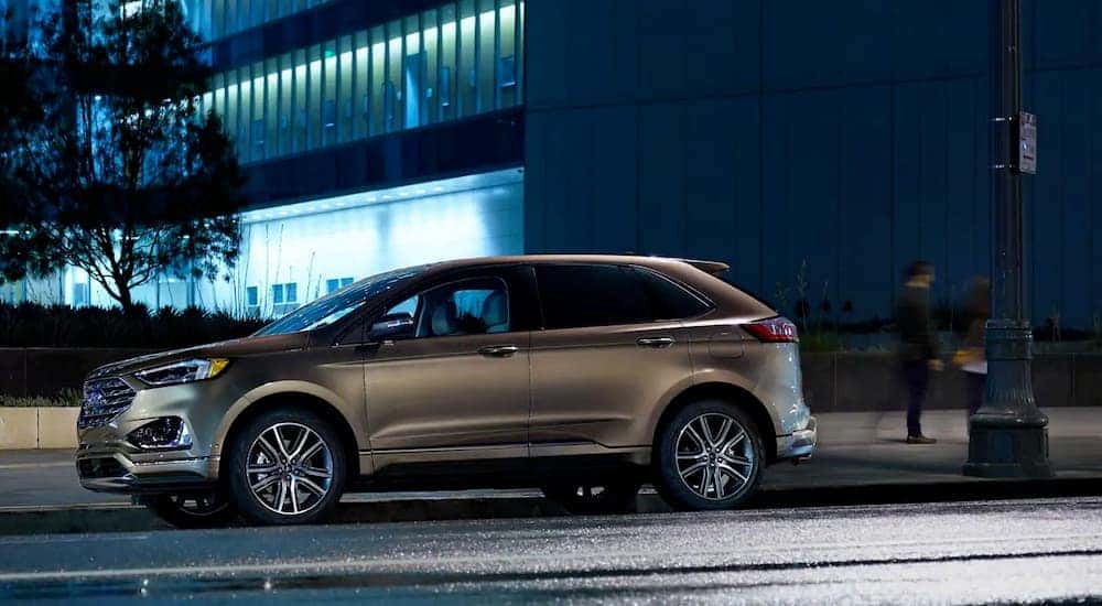 A tan 2019 Ford Edge, one of the popular Ford SUVs for sale, is parked outside a lighted building at night.