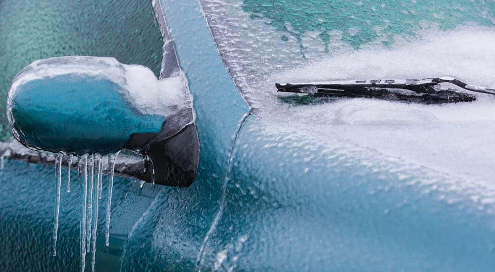 A closeup is shown of a blue car covered in ice in Cincinnati, OH.