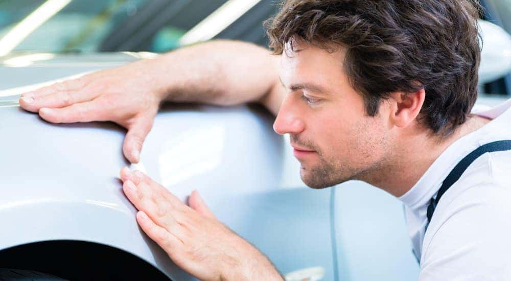A man is checking the body panel of a car while shopping for used cars in Cincinnati, OH.