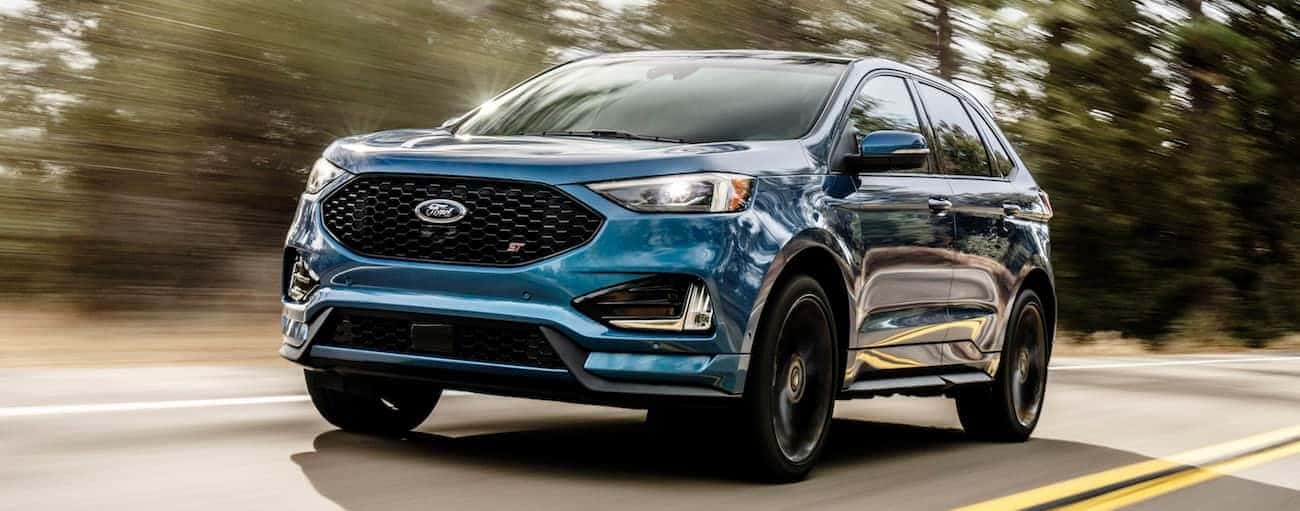 A blue 2019 Ford Edge ST, which wins when comparing the 2019 Ford Edge vs 2019 Honda Passport, is driving on a tree-lined road.