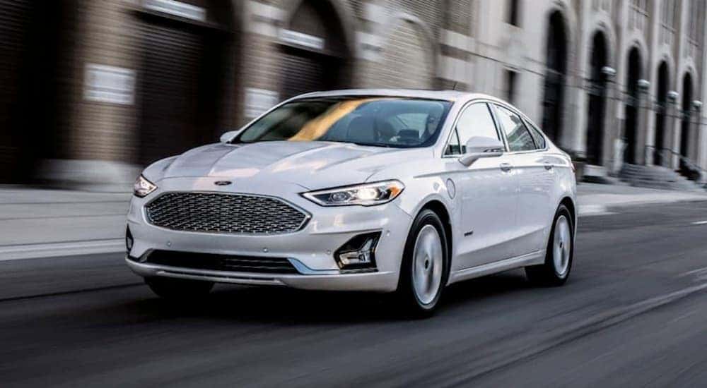 A white 2019 Ford Fusion is driving past city buildings near Cincinnati, OH
