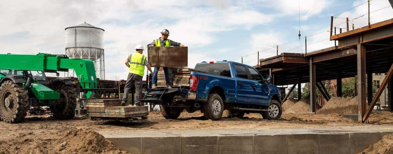 Workers are loading a blue 2020 Super Duty Ford F-250 at a construction site.