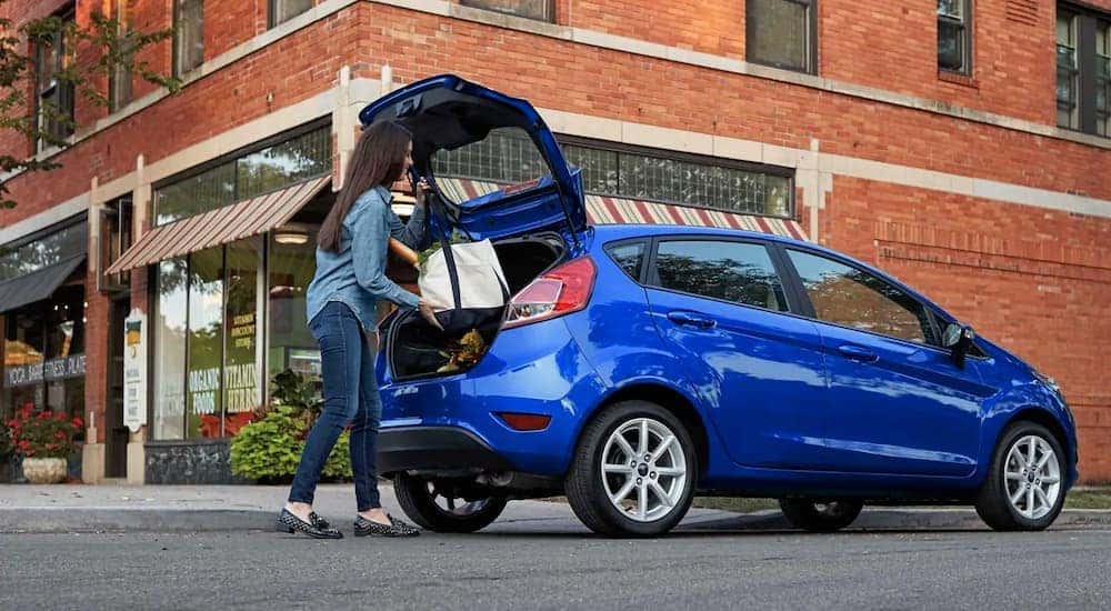 A woman is putting bags into the trunk of her blue 2019 Ford Fiesta.