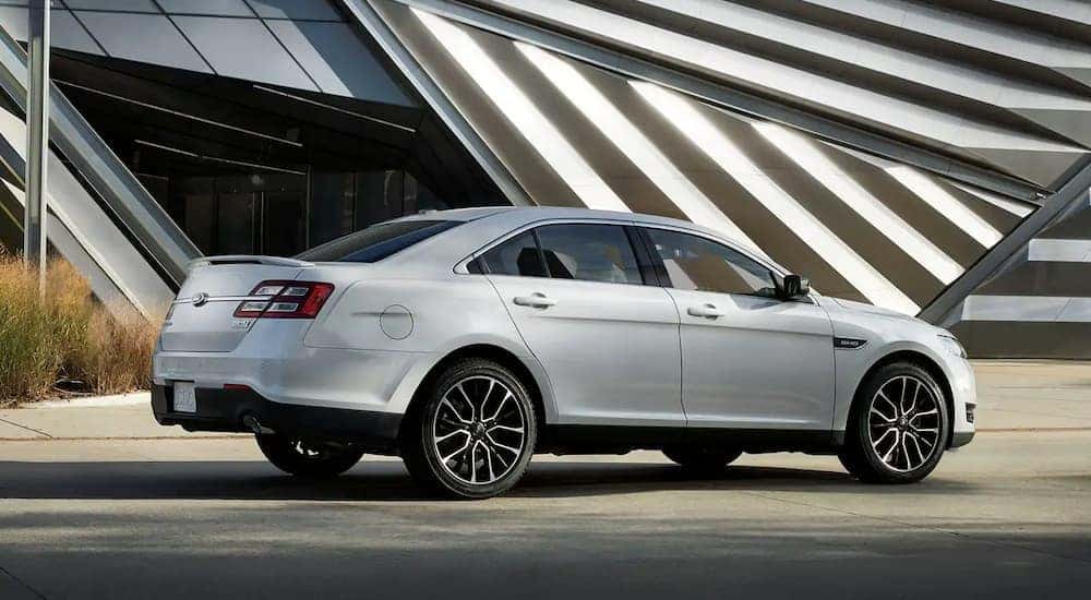 A silver 2019 Ford Taurus is parked in front of a white building on a sunny day.