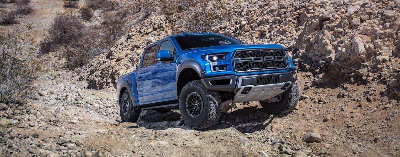 A blue 2019 Ford Raptor is on a rocky trail in the desert.