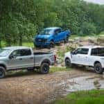 Three of the 2020 Ford Super Duty trucks are parked on a muddy trail off-road.