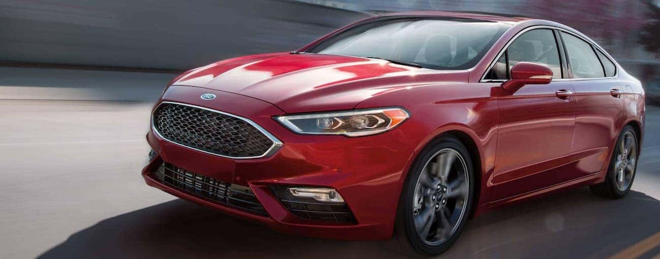 A red 2019 Ford Fusion is driving on a highway.