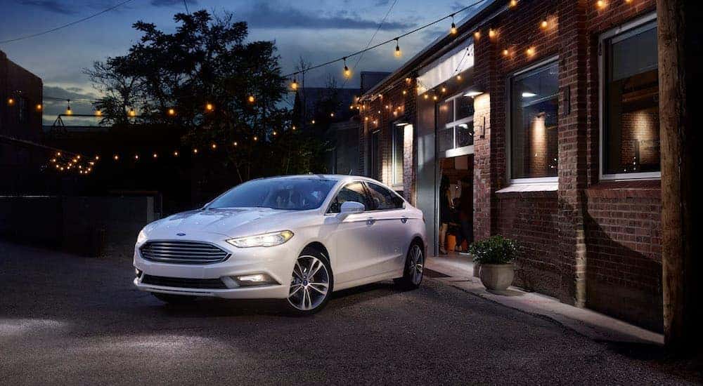 A white 2017 Ford Fusion, a popular option among used cars in Cincinnati, OH, is parked in front of a restaurant during dusk. 