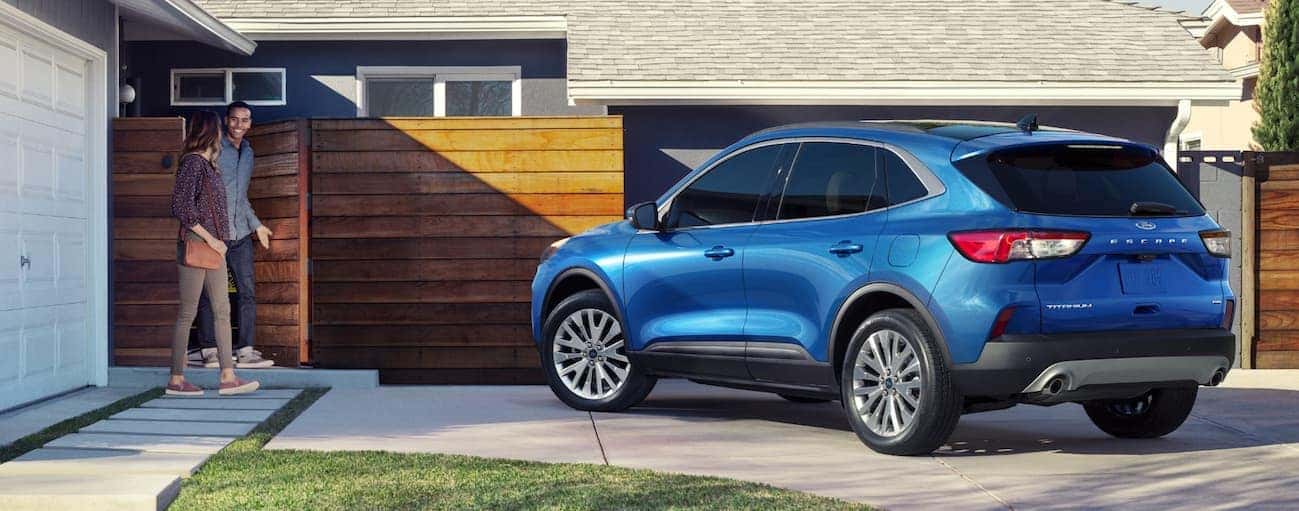 A smiling couple is walking to their all-new blue 2020 Ford Escape that's parked in a driveway near Cincinnati, OH.