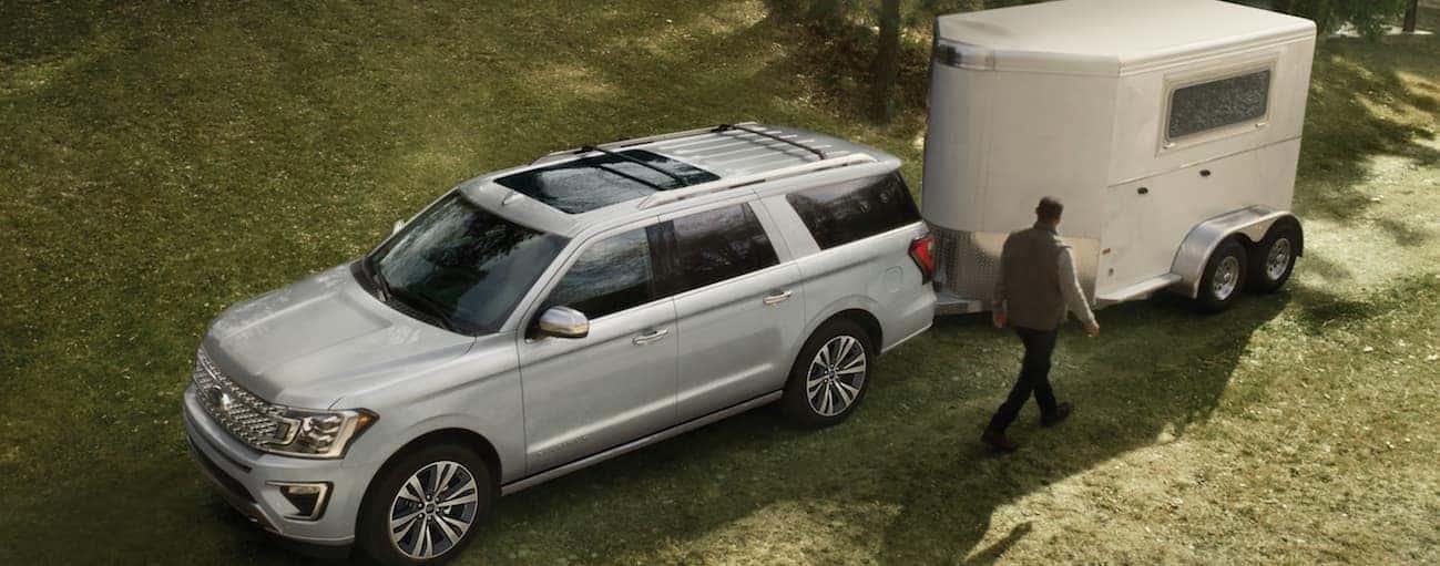 A silver 2020 Ford Expedition is parked in grass while towing a large horse trailer.