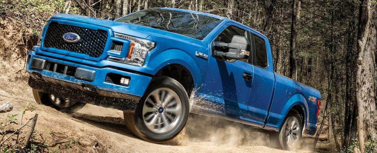 A blue 2020 Ford F-150 is driving on a dirt trail through the woods near Cincinnati, OH.